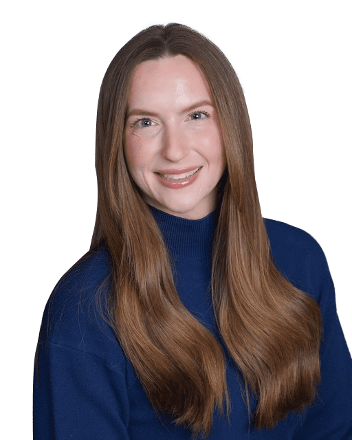 A person with long brown hair smiles while wearing a blue sweater against a neutral background.